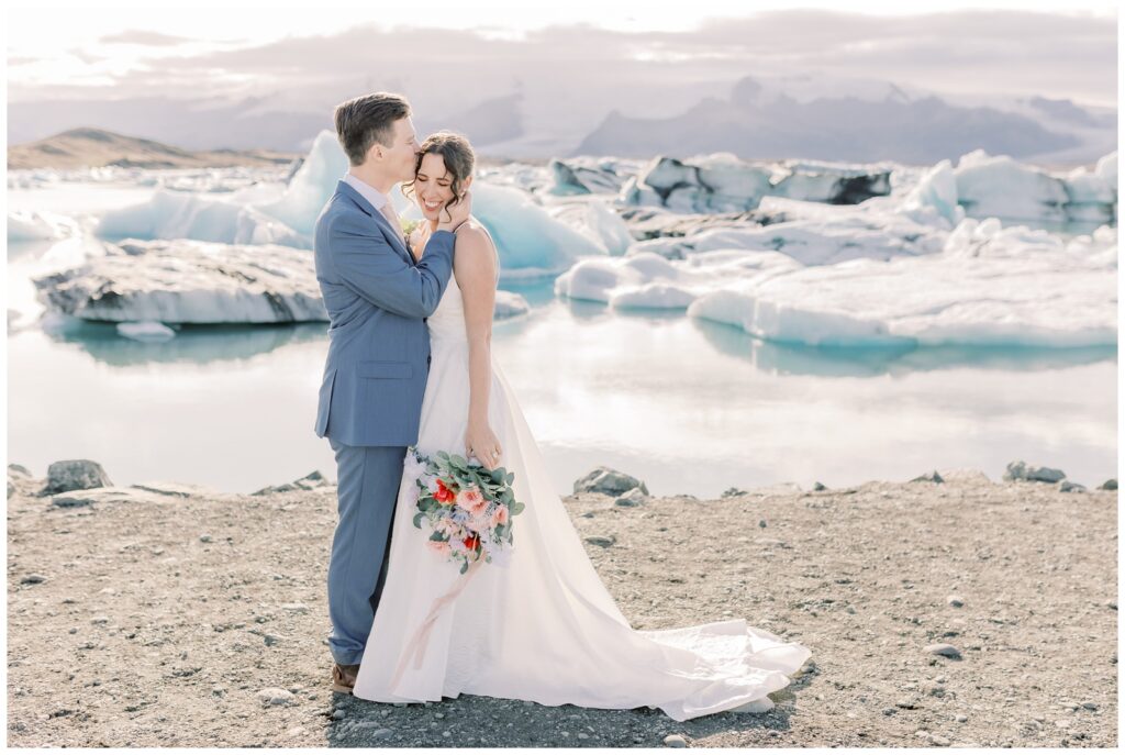 Couple kissing on their wedding day in front of the water and glaciers in Glacier Lagoon in Iceland.
