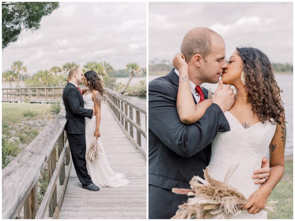 Interracial couple kissing on their wedding day on a boardwalk with palm trees in the background.
