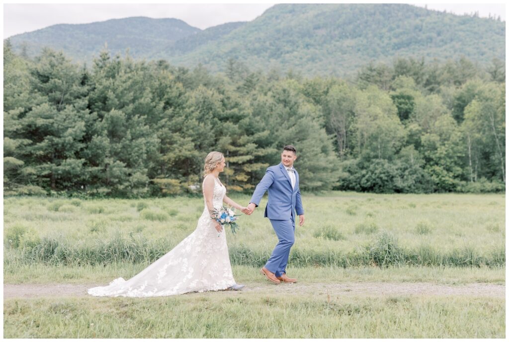 Couple walking hand in hand on their wedding day in Marcy Field with an Adirondack Mountain in the background.
