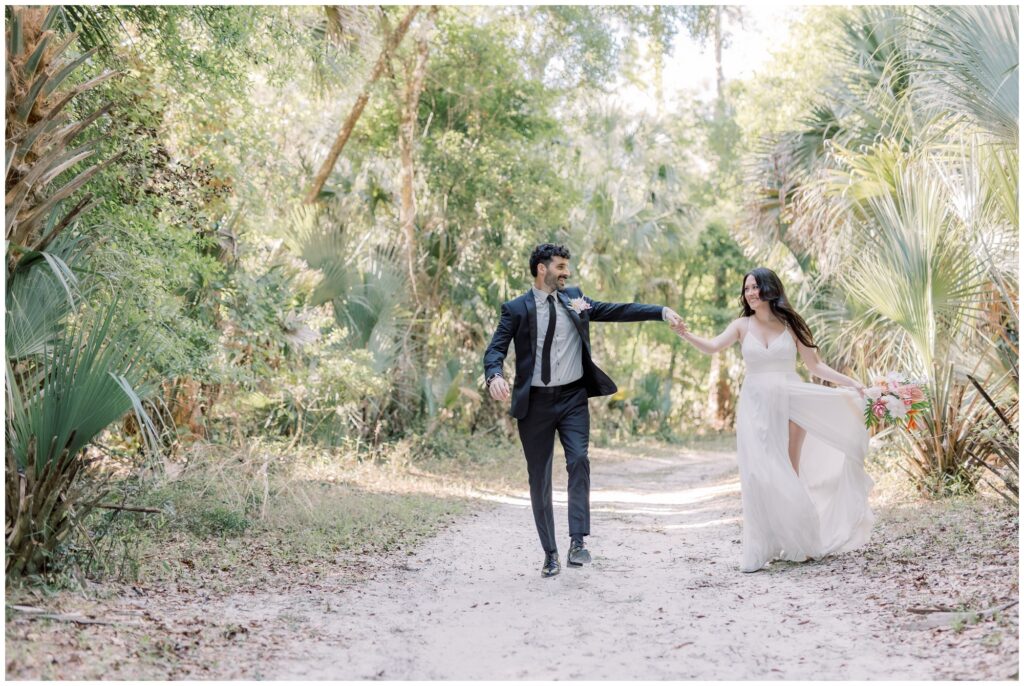 Couple running down a forest path holding hands during their elopement at Rock Springs in Apopka, Florida.